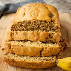 a loaf of banana bread sitting on top of a wooden cutting board next to a ripe banana