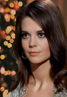 a woman with dark hair and blue eyes is posing for a photo in front of a christmas tree