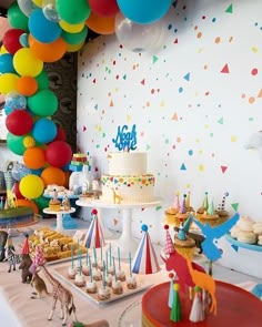 a birthday party with colorful balloons, cake and cupcakes on the table in front of it