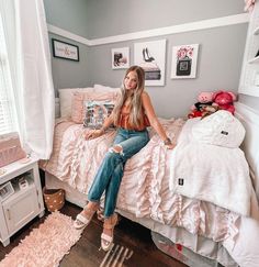 a woman sitting on top of a bed next to a white dresser and pink bedspread