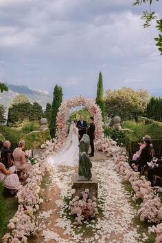 a couple getting married in front of an arch with flowers on it and people sitting at the end