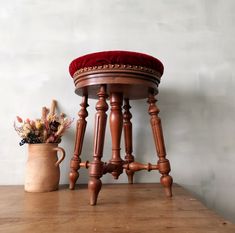 a wooden stool with a red cushion on it and a flower pot next to it