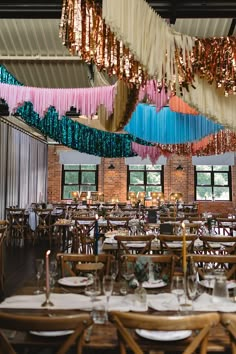 the tables and chairs are set up for an event with colorful streamers hanging from the ceiling