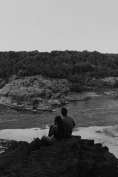 black and white photograph of two people sitting on rocks by the water looking out to sea