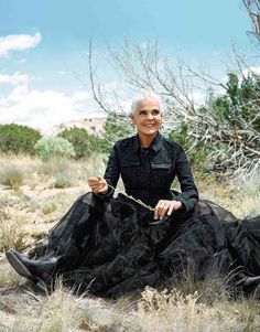 a woman sitting in the middle of a field wearing a black dress and holding a chain