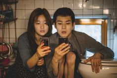 two people sitting on a toilet looking at their cell phones