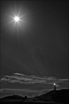 the sun shines brightly in the night sky over a lighthouse on top of a hill