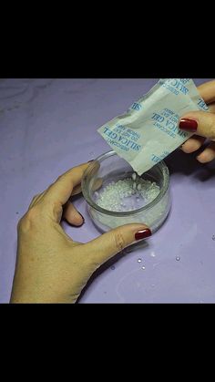 two hands holding a packet of powder over a glass bowl filled with water and white flakes