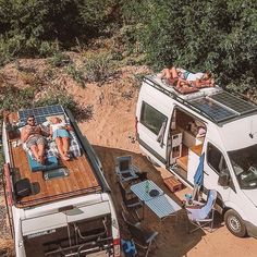 two people laying in the back of a van on top of a dirt road next to trees