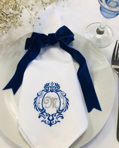 a white plate topped with a blue ribbon and a monogrammed napkin on top of it