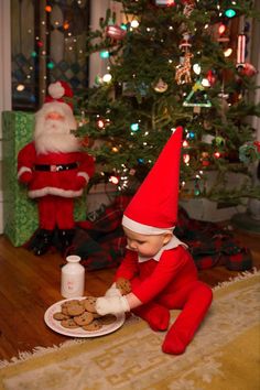 an elf is eating cookies in front of a christmas tree