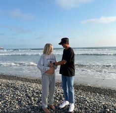 a man standing next to a woman on top of a sandy beach near the ocean