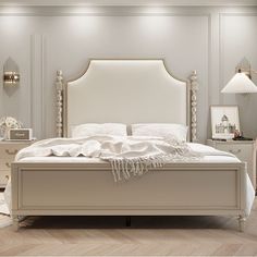 a large white bed sitting inside of a bedroom next to a night stand and lamp