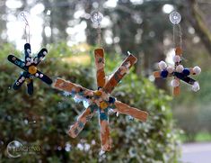 three snowflakes hanging from strings in front of trees and bushes with beads attached to them