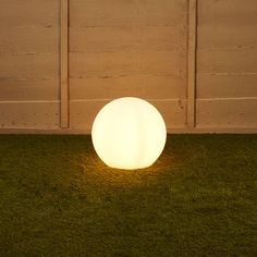 an illuminated ball sitting in the grass next to a fence