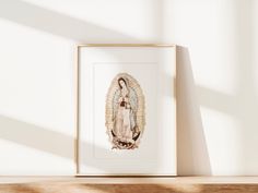 an image of the virgin mary on display in a wooden frame against a white wall