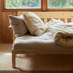 a bed with two pillows on top of it in front of a wooden wall and window