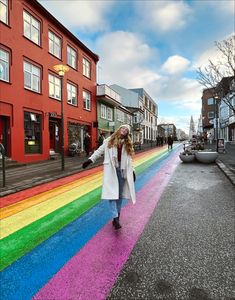 a woman is walking down the street in front of a rainbow painted wall and buildings