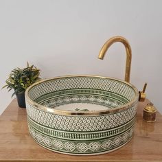 a green and white bowl sink sitting on top of a wooden counter next to a potted plant