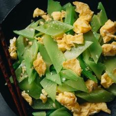 a black plate topped with eggs and green beans next to chopsticks on a table