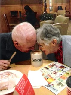 an older couple kissing each other at a table with food and drinks in front of them