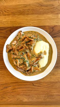 a white bowl filled with meat and gravy on top of a wooden table