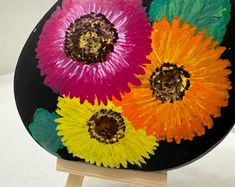 three colorful flowers on a black plate with wooden stand and white wall behind the plate