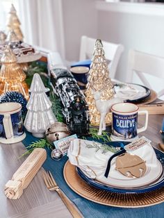 a dining room table set for christmas with blue and white plates, silverware, and trees