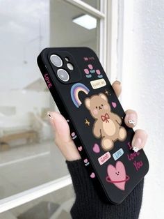 a woman holding up a phone case with a bear and rainbows on it in front of a window