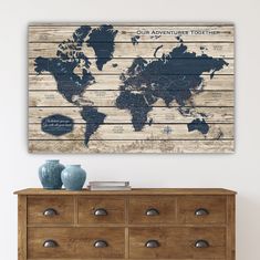 an old world map is mounted on a wooden wall above a dresser with two vases