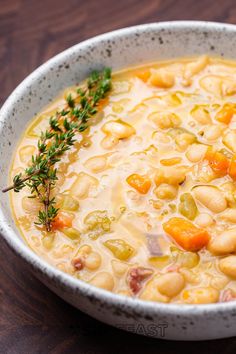 a white bowl filled with beans and carrots on top of a wooden table next to a spoon