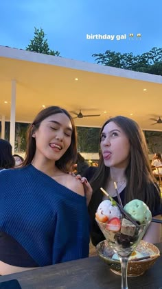 two women standing next to each other at a table with ice cream and fruit in it