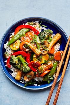 a blue bowl filled with vegetables and rice next to chopsticks on a table