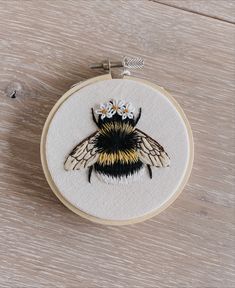 a small embroidered bee with daisies on it's head sitting on a wooden surface