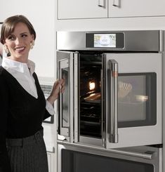 a woman holding an oven door open in a kitchen with white cabinets and stainless steel appliances