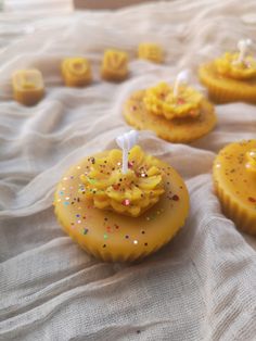 some yellow cupcakes with candles are on a white cloth and have sprinkles