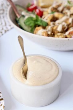 a salad with dressing in a bowl next to a fork on a white tablecloth