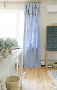 a room with a wooden floor and blue curtains on the window sill next to a white dresser