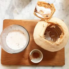 a wooden cutting board topped with food and a bowl filled with liquid next to it