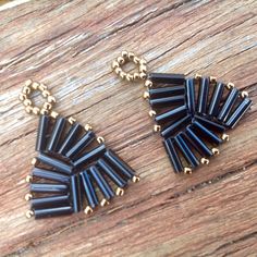 two pairs of black and gold earrings sitting on top of a wooden table next to each other