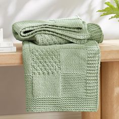 a green knitted blanket sitting on top of a wooden table next to a plant