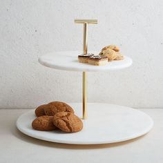 two desserts sitting on top of a white cake stand with gold handles and small cookies