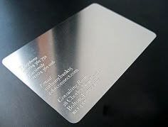 a close up of a metal business card on a black surface with silver foil and white lettering