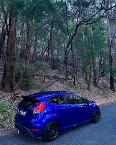 the blue car is parked on the side of the road in front of some trees