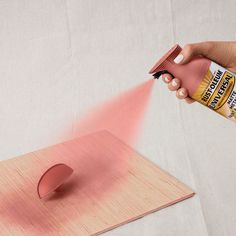 a person spraying pink paint onto a piece of wood