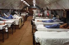 there are many people laying in the beds inside this hospital room with lights hanging from the ceiling