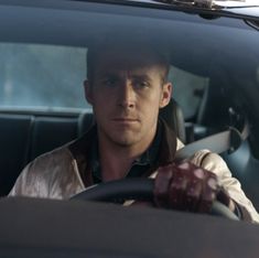 a man sitting in the driver's seat of a car with his hand on the steering wheel