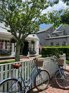 two bicycles parked next to each other on a brick walkway in front of a white picket fence