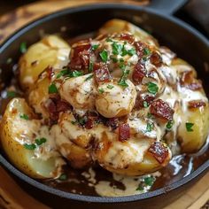 a skillet filled with potatoes covered in bacon and cheese sauce on top of a wooden cutting board