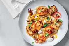 a white plate topped with tofu and veggies on top of a table